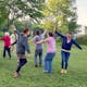Eine Gruppe bewegt sich lachend mit gehobenen Armen in einem Park