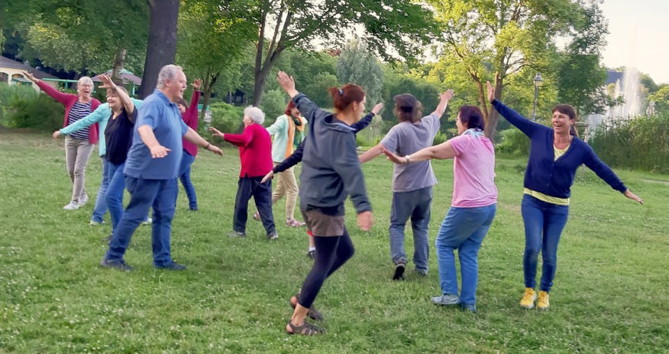 Eine Gruppe bewegt sich lachend mit gehobenen Armen in einem Park